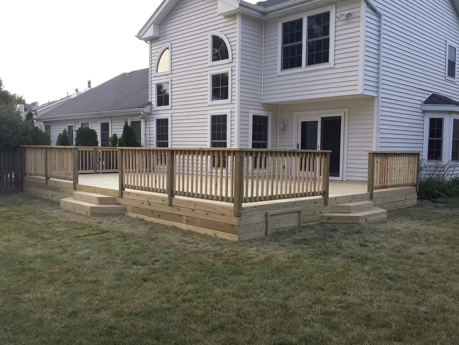 Wraparound wood deck with picket railing on a two-story home